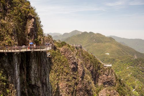 Free Breathtaking view of a cliffside footbridge winding through lush mountain landscapes under a clear sky. Stock Photo