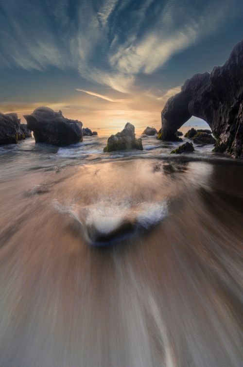 Free Dynamic ocean scene with rock arches and vivid sky at sunset, showcasing nature's power and beauty. Stock Photo