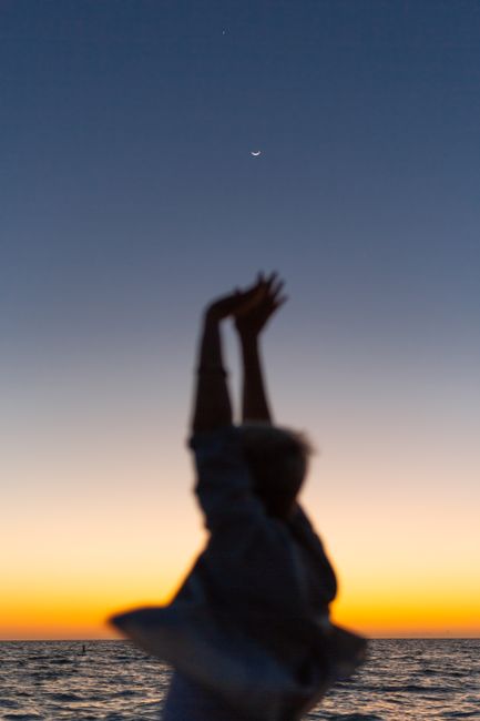 A serene silhouette of a person stretching under the crescent moon at sunset by the sea.