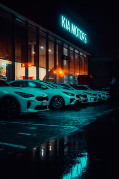 夜间，起亚汽车展厅灯火通明，停放的汽车倒映在潮湿的人行道上