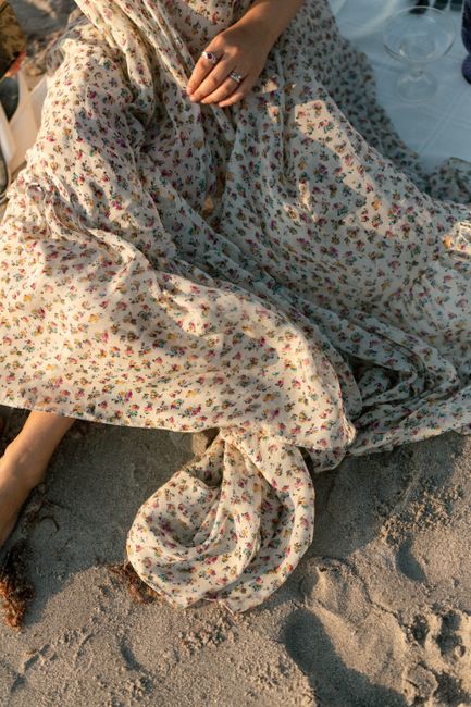 A woman in a floral dress sitting on beach sand, captured from above.
