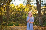 一个金发女孩在阳光明媚的秋日里，手拿一根棍子，微笑着站在森林中，四周满是秋叶