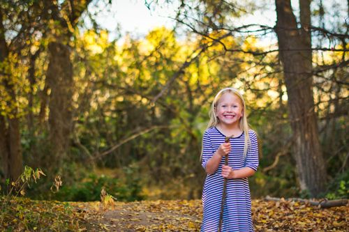 Free A smiling blonde girl enjoys a sunny fall day outdoors in a forest, holding a stick and surrounded by autumn leaves. Stock Photo
