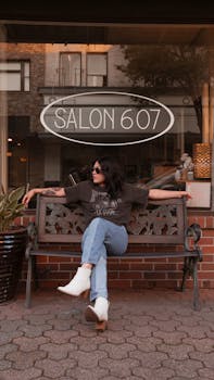 Woman in casual attire poses on a bench outside Salon 607, stylish and relaxed.