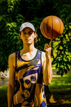 A young man skillfully spins a basketball on his finger in a sunny park, showcasing athletic ability and sportsmanship.