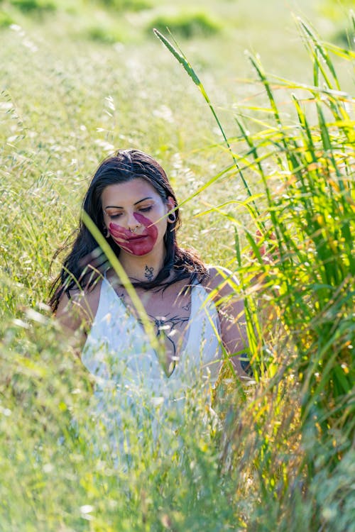 Молодая женщина с красным отпечатком руки на лице сидит в высокой траве