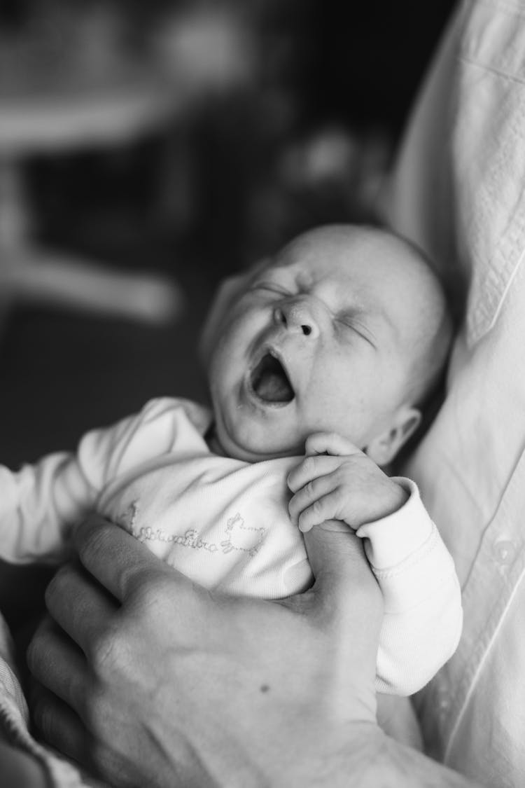 Black And White Photo Of Hands Holding Yawning Baby