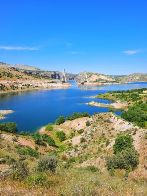Free Breathtaking landscape of a serene lake with a bridge and surrounding hills under a clear sky. Stock Photo