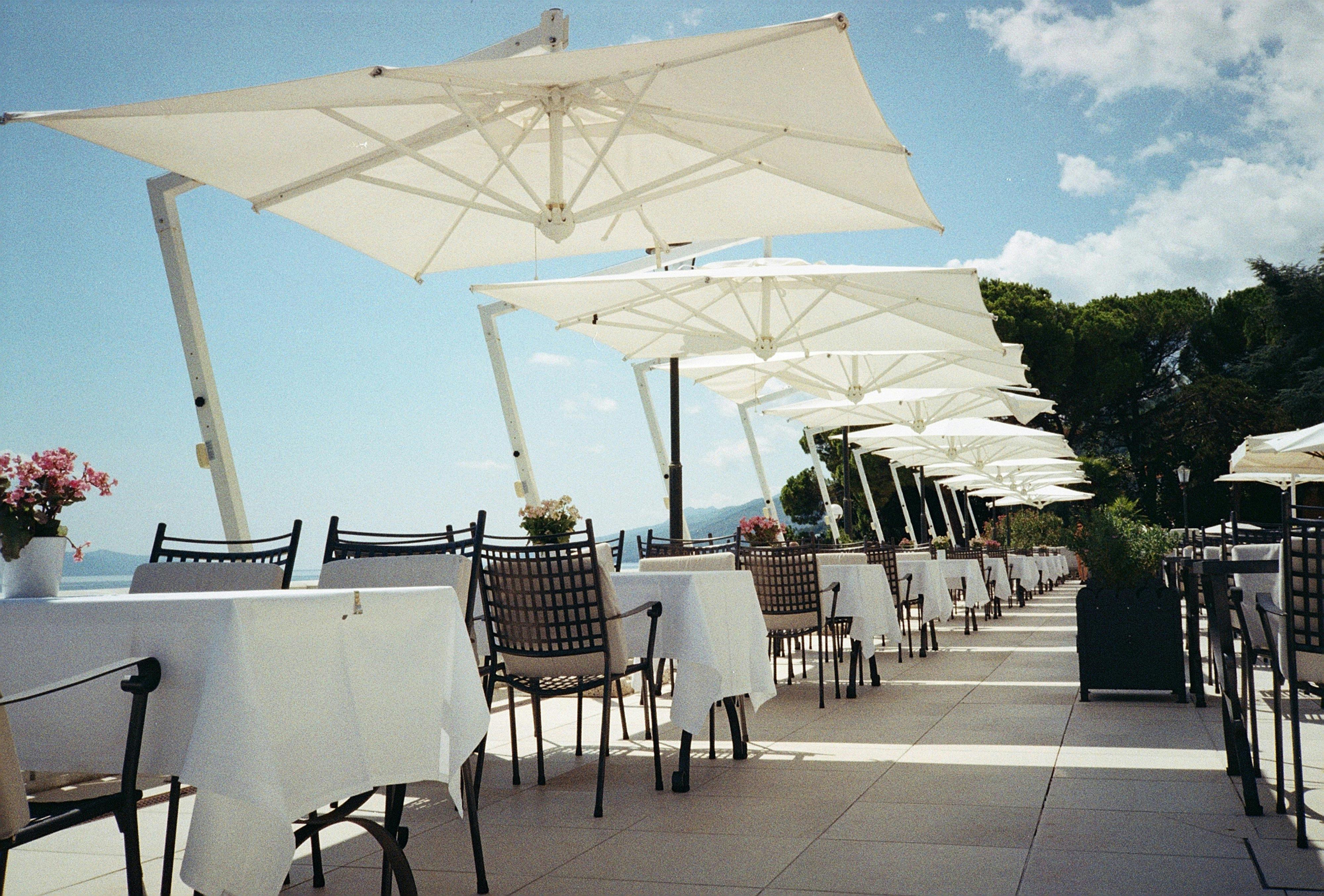 Coastal restaurant terrace with white umbrellas and empty tables, a perfect summer day.