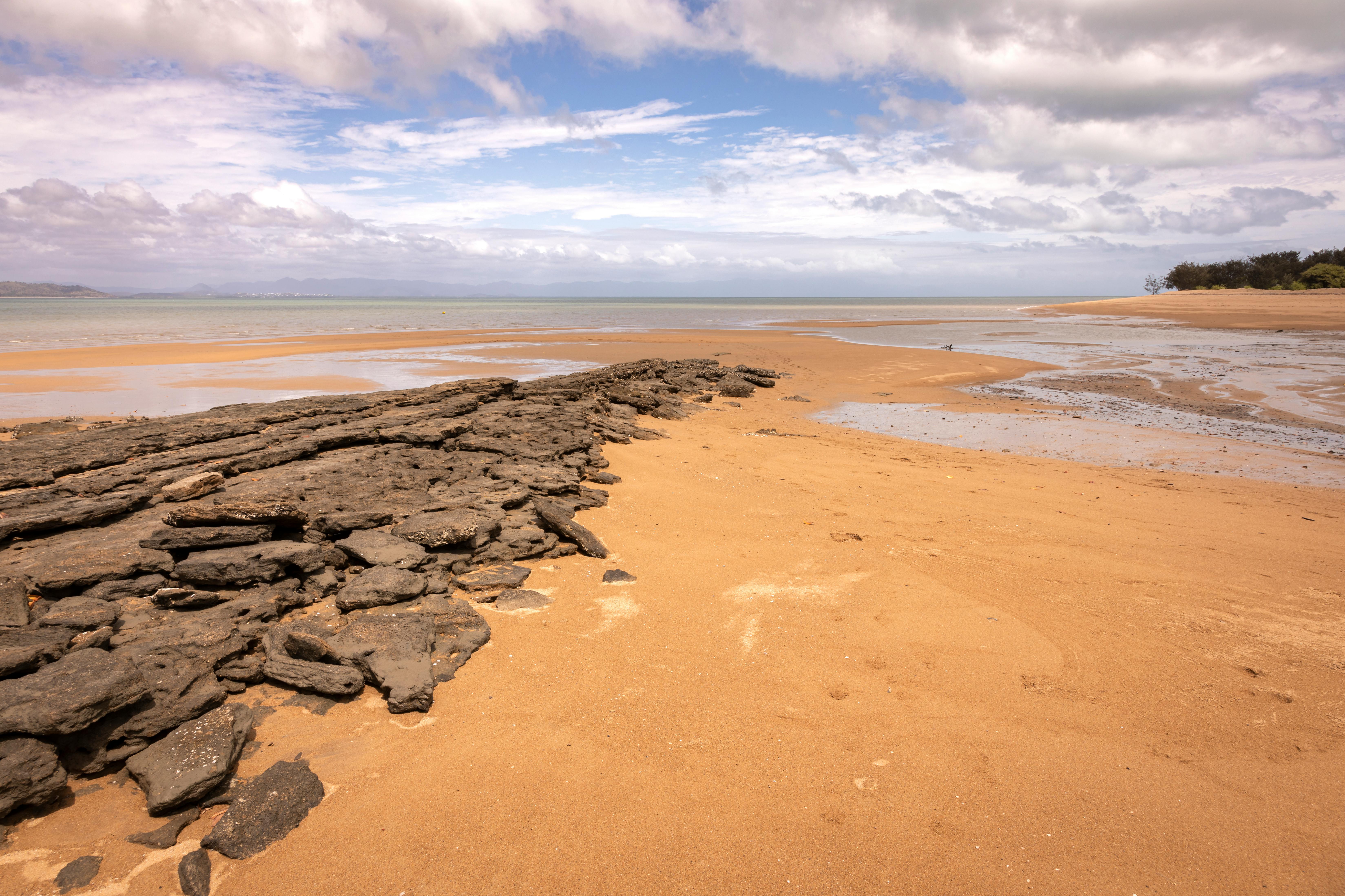 Calm beach scene with rocky shoreline under a partly cloudy sky.