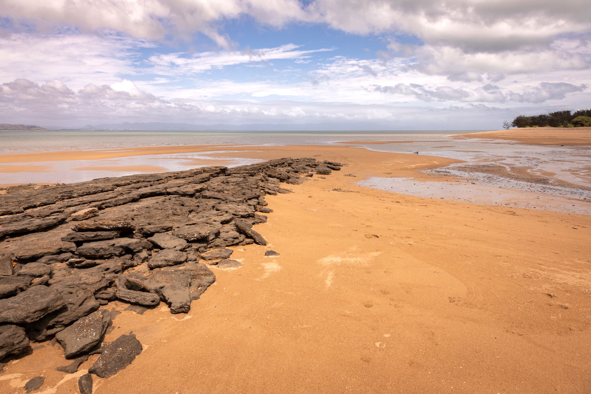 Calm beach scene with rocky shoreline under a partly cloudy sky.