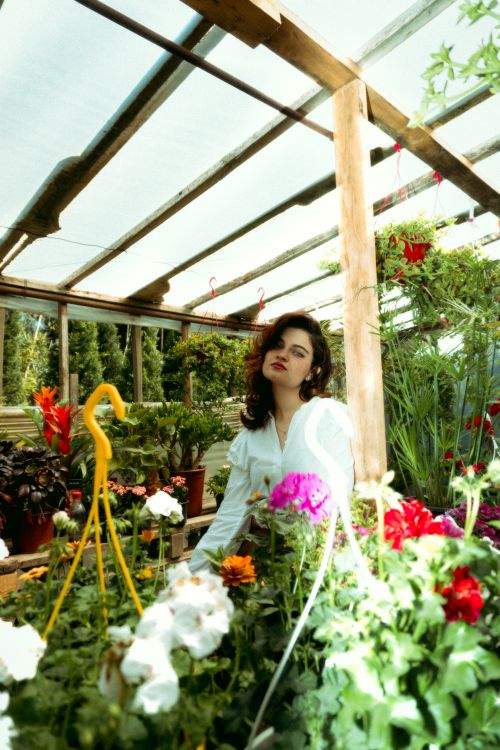 Free Elegant woman in white amidst colorful flowers in a greenhouse, capturing natural beauty. Stock Photo