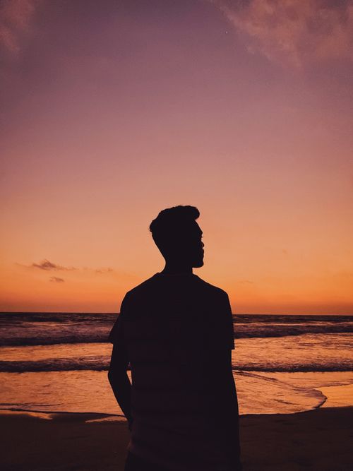 Free A silhouette of a man standing on a beach at sunset in GA, India with vibrant pink skies. Stock Photo