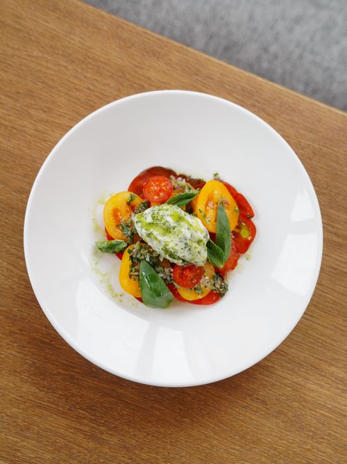 Free Delicious fresh tomato salad topped with basil and green herb dressing in a white bowl. Stock Photo