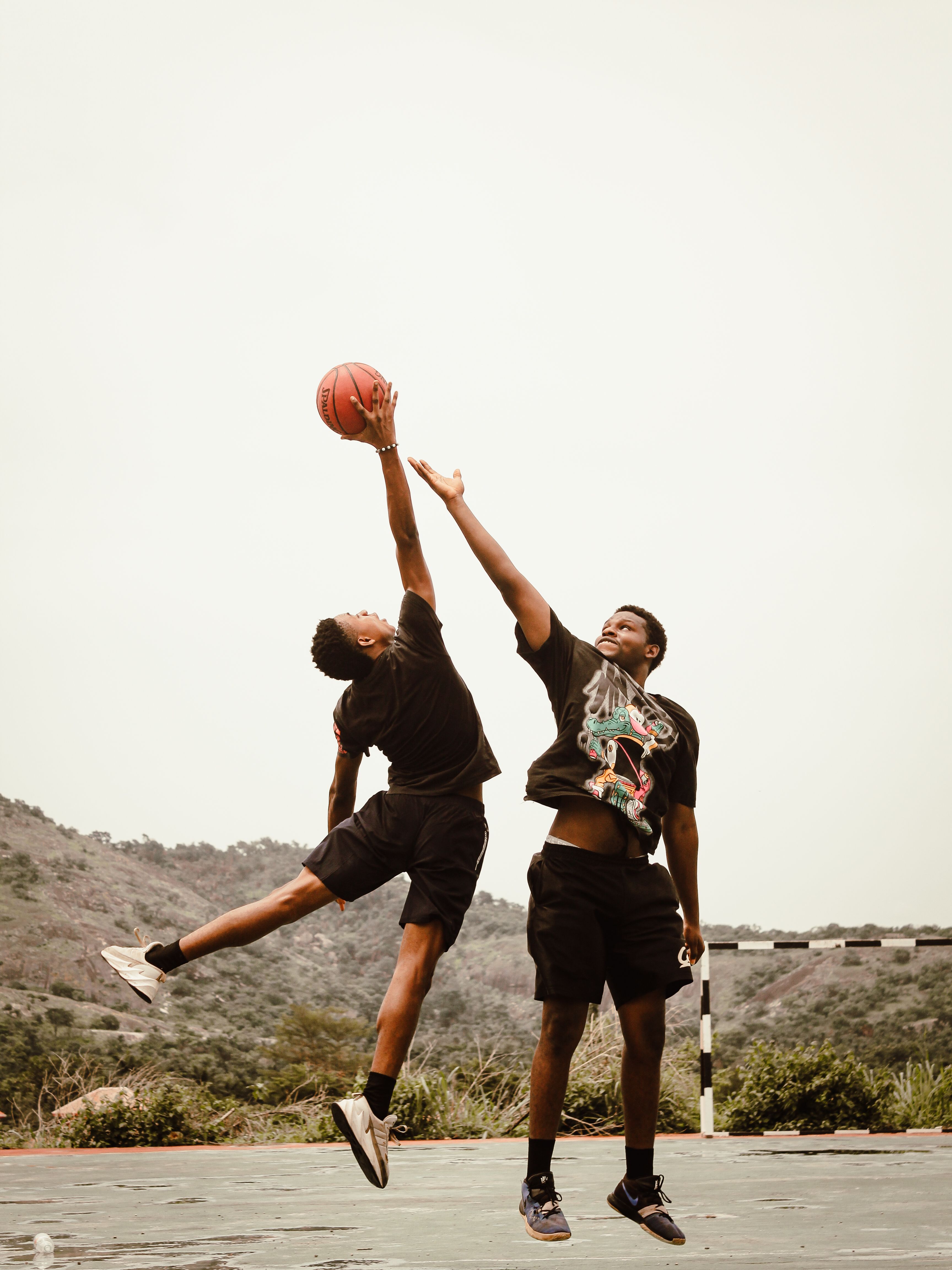 Two young men in a competitive basketball game outdoors with scenic background.