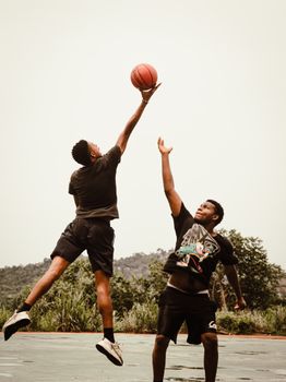 Two men playing basketball outdoors, showcasing athleticism and joy on the court.