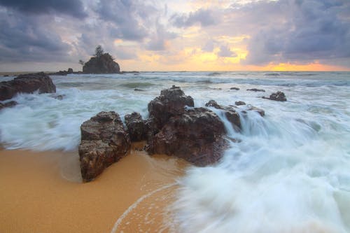 Roca En La Orilla De La Playa Con Olas Rompiendo Durante El Cielo Nublado Durante El Día