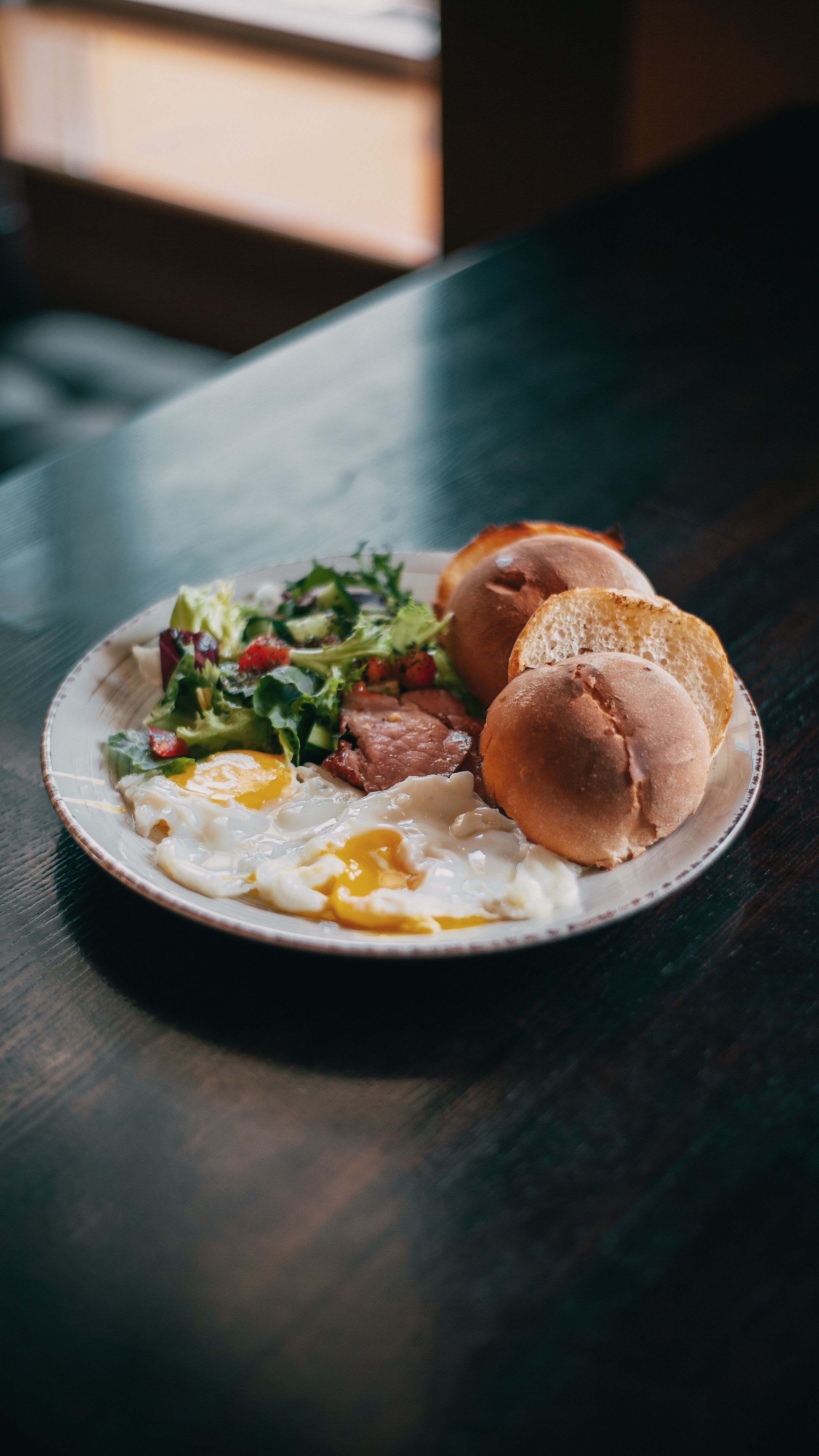 A hearty breakfast of sunny-side-up eggs, fresh salad, and buns on a rustic table.