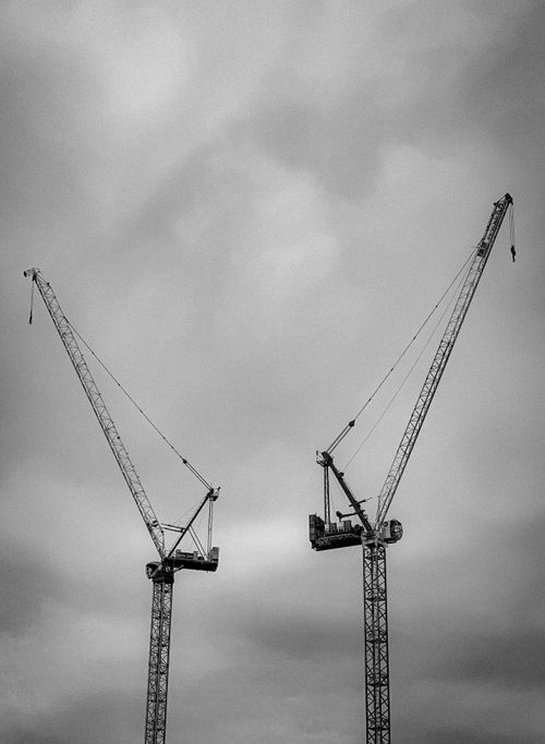 Free Black and white image of towering cranes at a construction site in Cardiff under a cloudy sky. Stock Photo