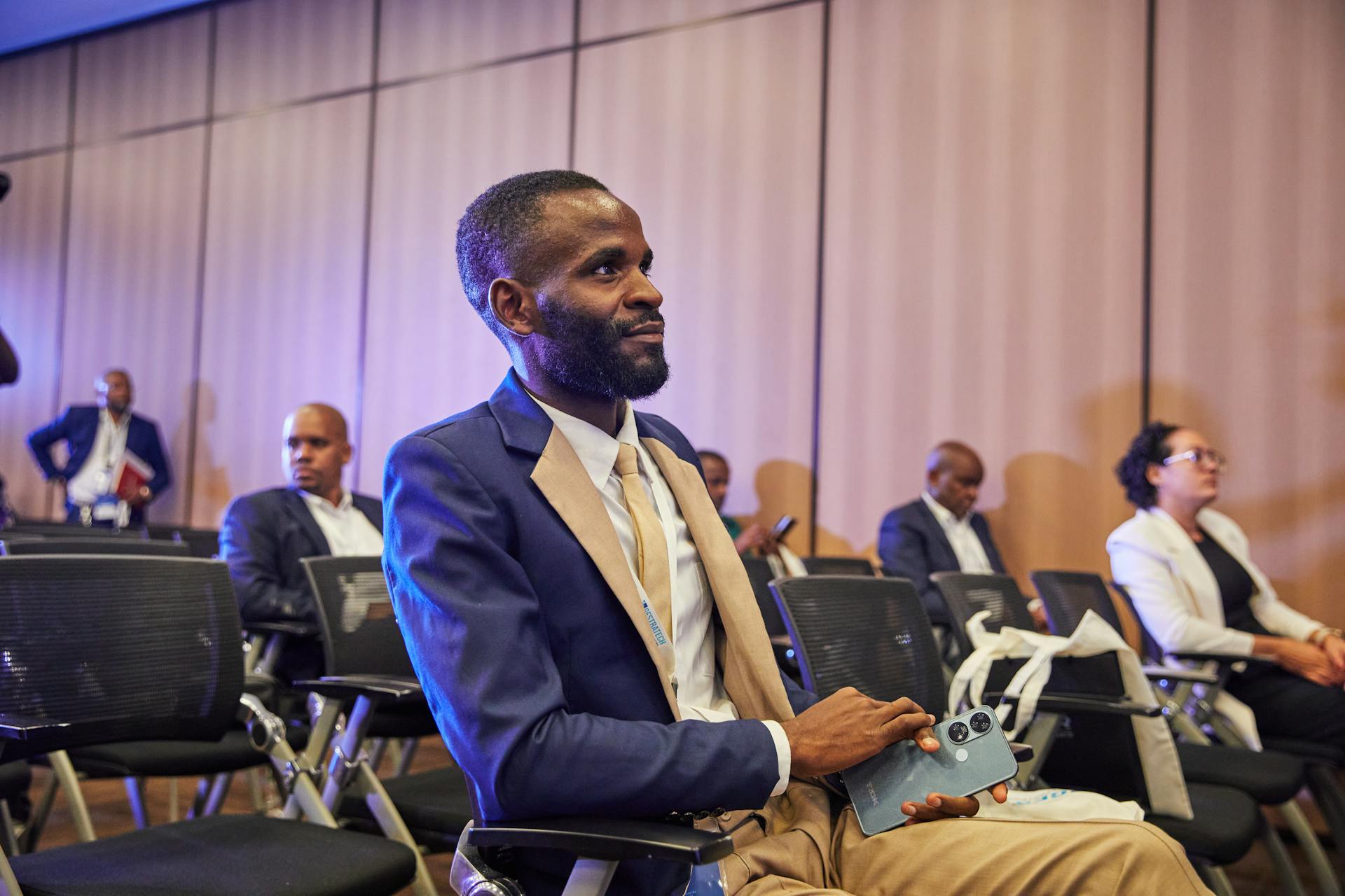 Business professional attending conference with focus, wearing suit and holding phone.