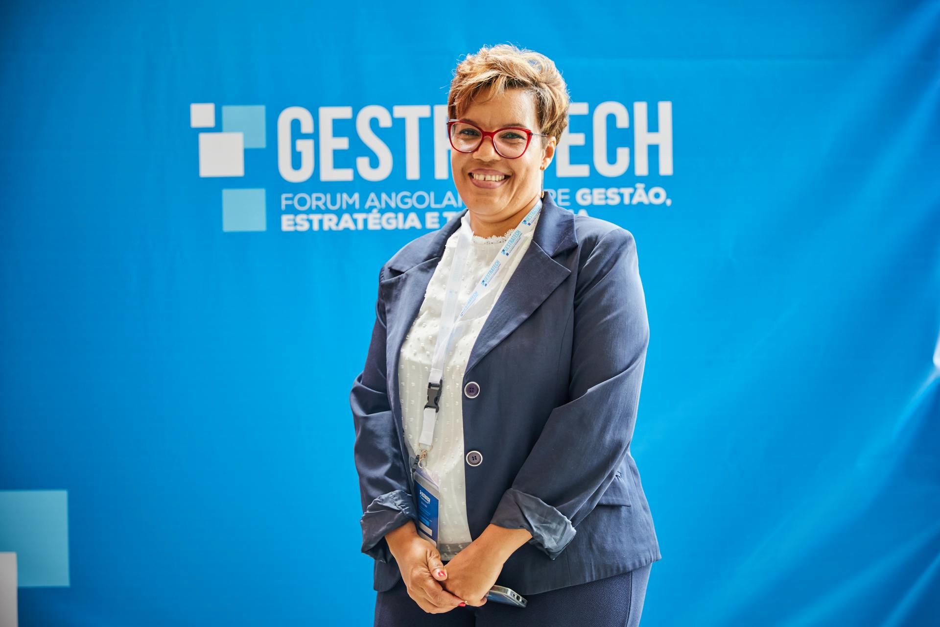 Businesswoman smiling in front of blue backdrop at trade fair event, embodying leadership and professionalism.