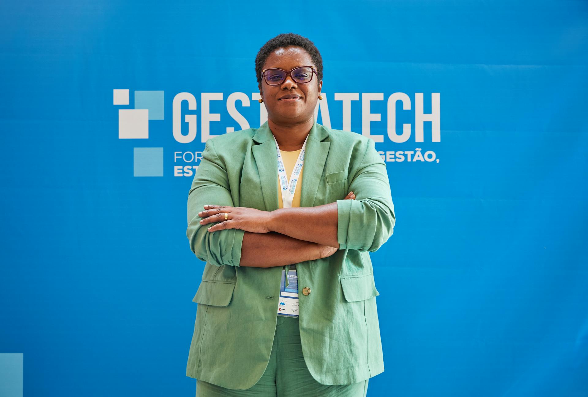 Confident woman in green suit poses at a trade event with a blue backdrop, exuding expertise and leadership.