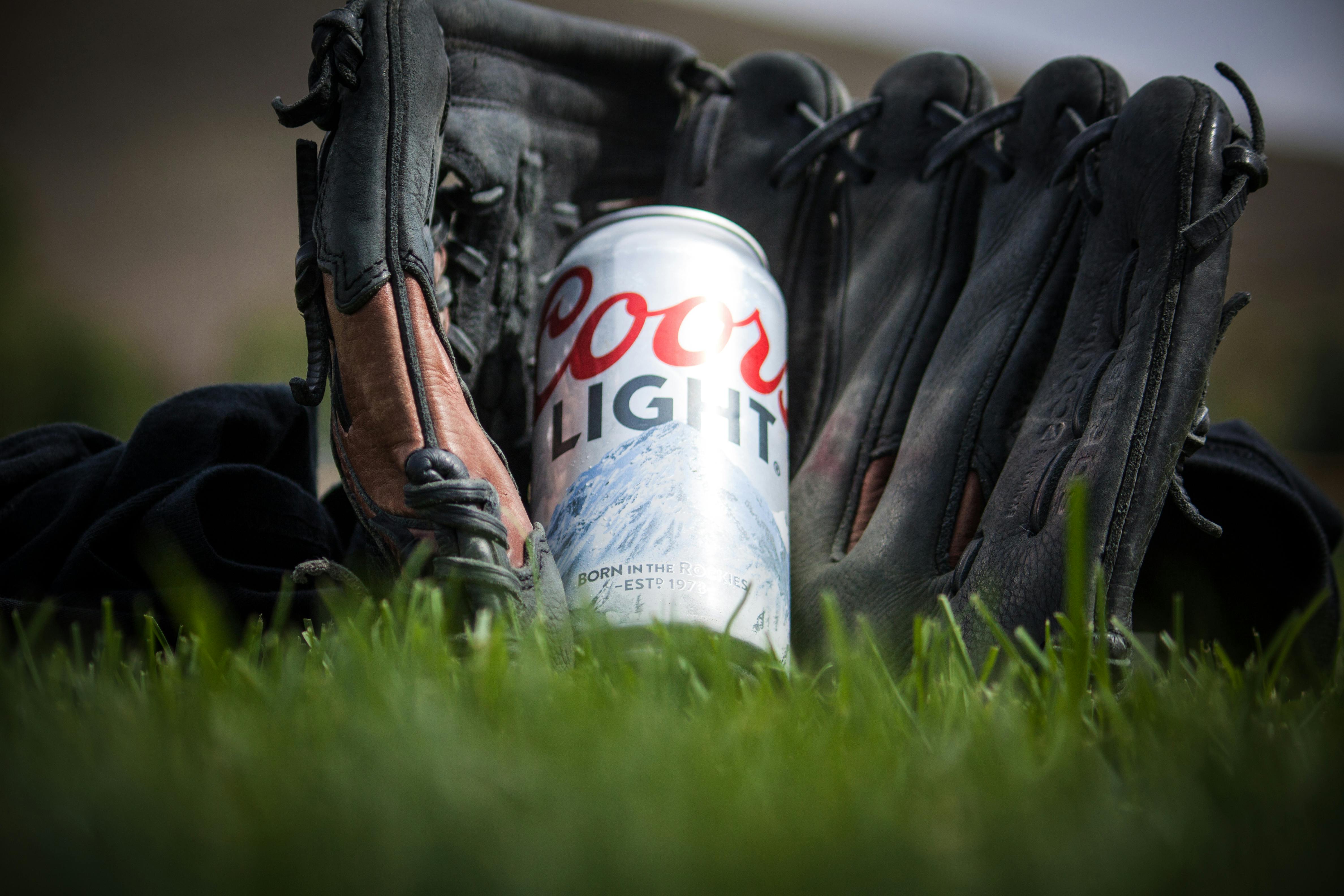 Close Up Photography of Coors Light Beer Near Black Baseball Mitts