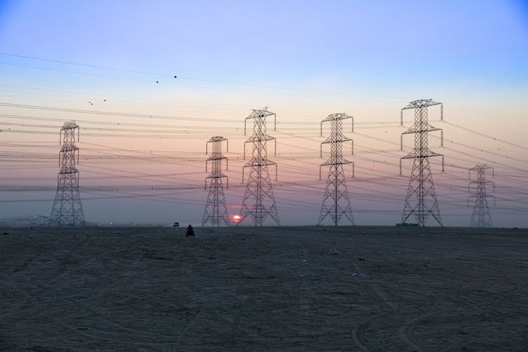 Electricity Poles And Lines On A Field At Sunset