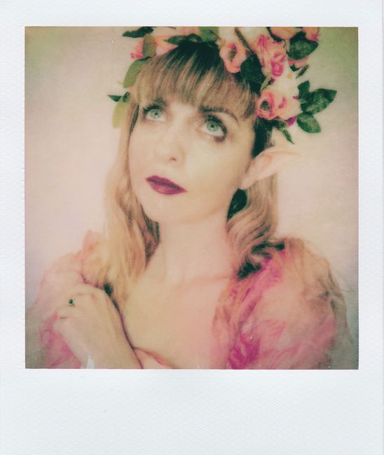 Artistic portrait of a woman with elf ears wearing a floral garland and a dreamy expression.
