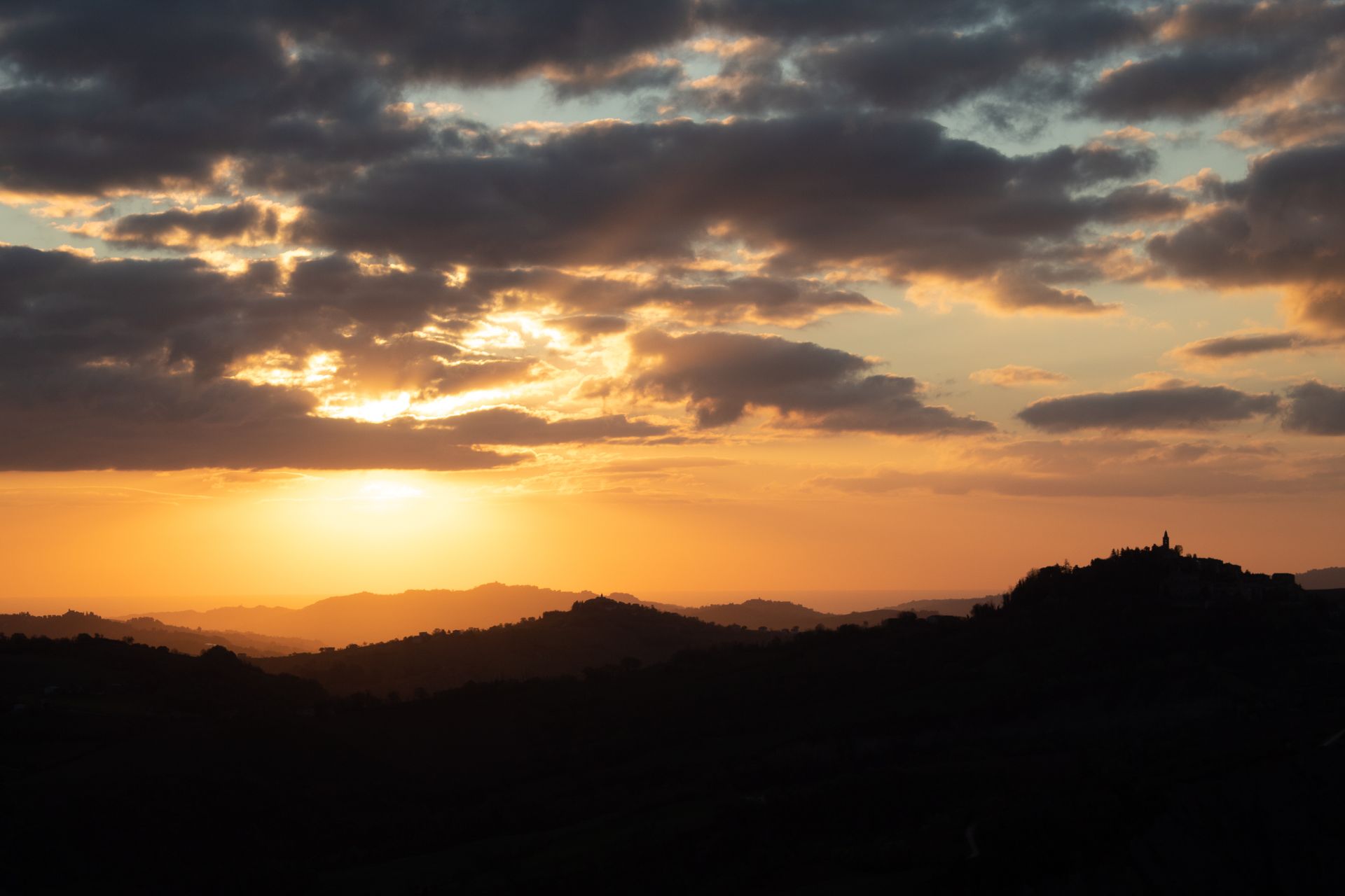 A stunning sunset over the hills of Santa Vittoria in Matenano, Italy, with dramatic clouds and landscape silhouettes.