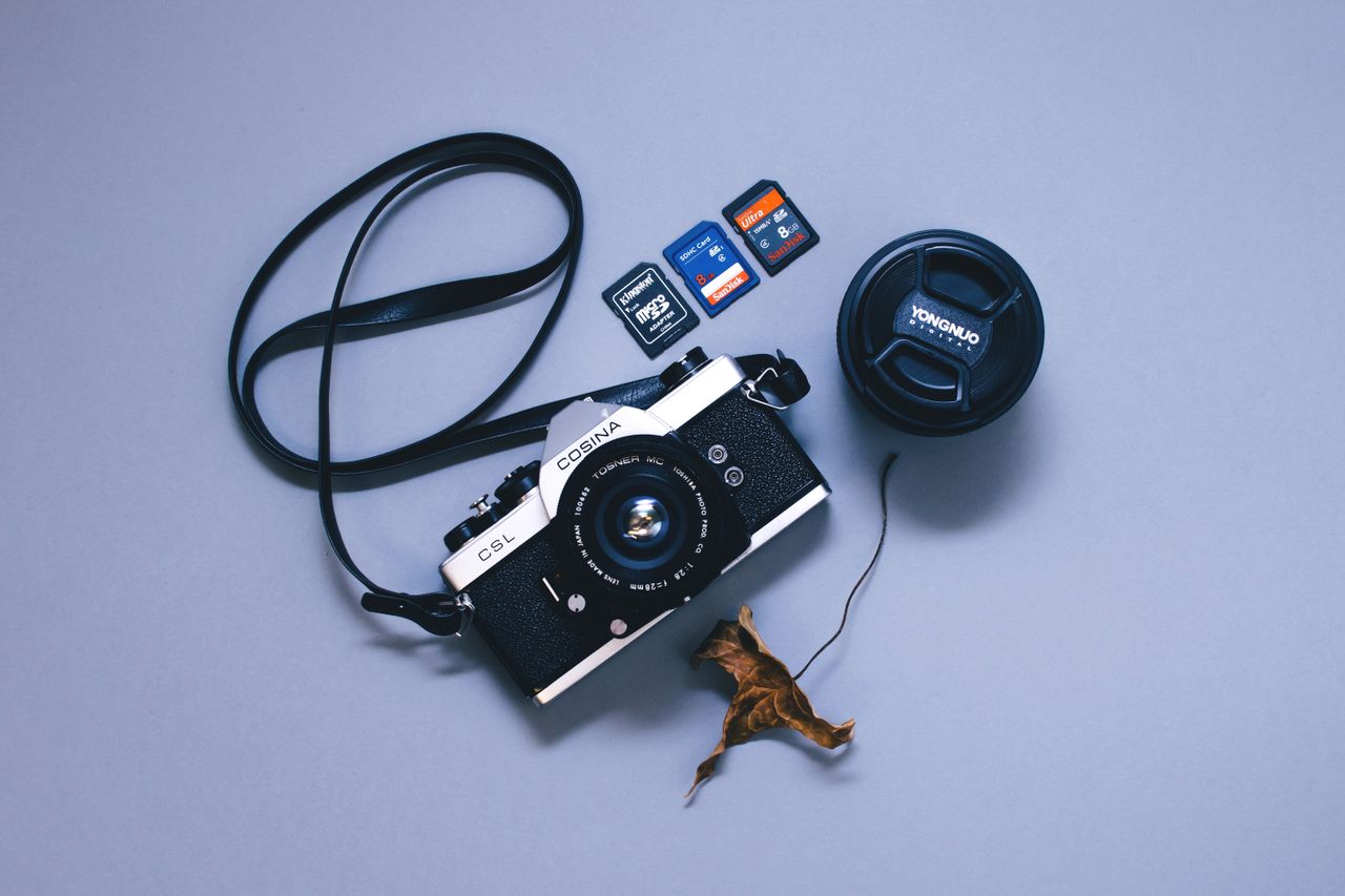 Flat lay of a vintage camera, memory cards, lens cap, and dry leaf.