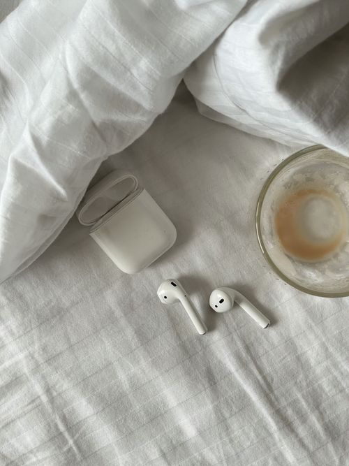 Free Serene overhead view of earbuds and coffee on white bedding, perfect for tech and lifestyle themes. Stock Photo