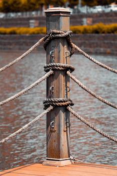 Close-up of a wooden post with ropes by a waterfront, conveying a nautical theme.