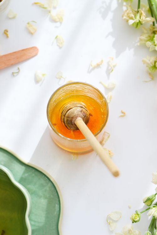 Free A vibrant top view of a honey dipper in glass jar surrounded by flowers on a bright white background. Stock Photo
