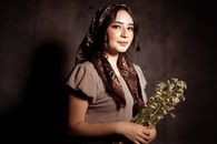 Elegant woman holding a bouquet, wearing a brown headscarf, in moody lighting.