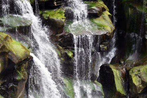 Free A picturesque waterfall cascading over moss-covered rocks in a tranquil natural setting. Stock Photo
