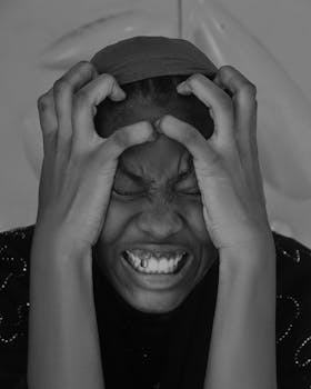 Black and white portrait showing a person deeply expressing emotion by clutching their head in distress.