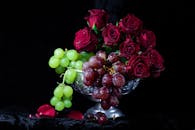 深色背景上点缀着鲜艳的红玫瑰和甜美的葡萄，这幅静物画令人惊叹