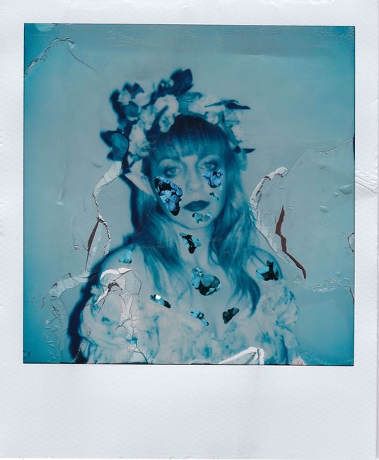 Unique blue-toned Polaroid portrait featuring a woman with a floral headpiece, artistically edited for a surreal feel.