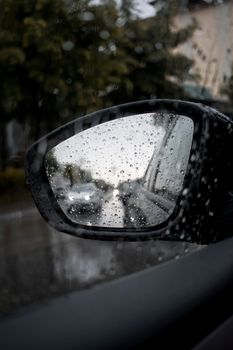 Close-up of raindrops on car mirror reflecting a rainy urban street scene.