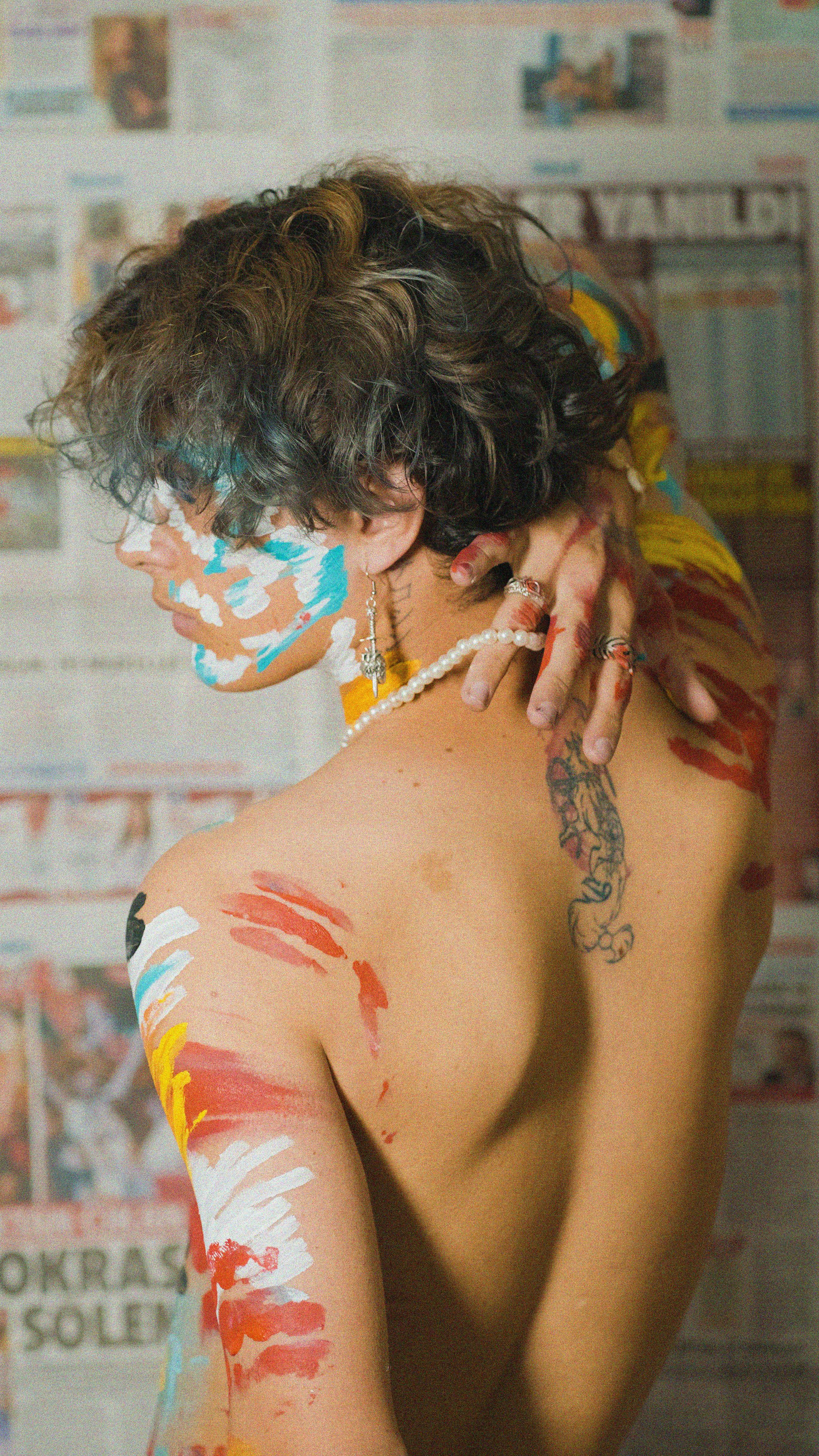 Shirtless model with painted body art and unique tattoo poses in front of newspapers.