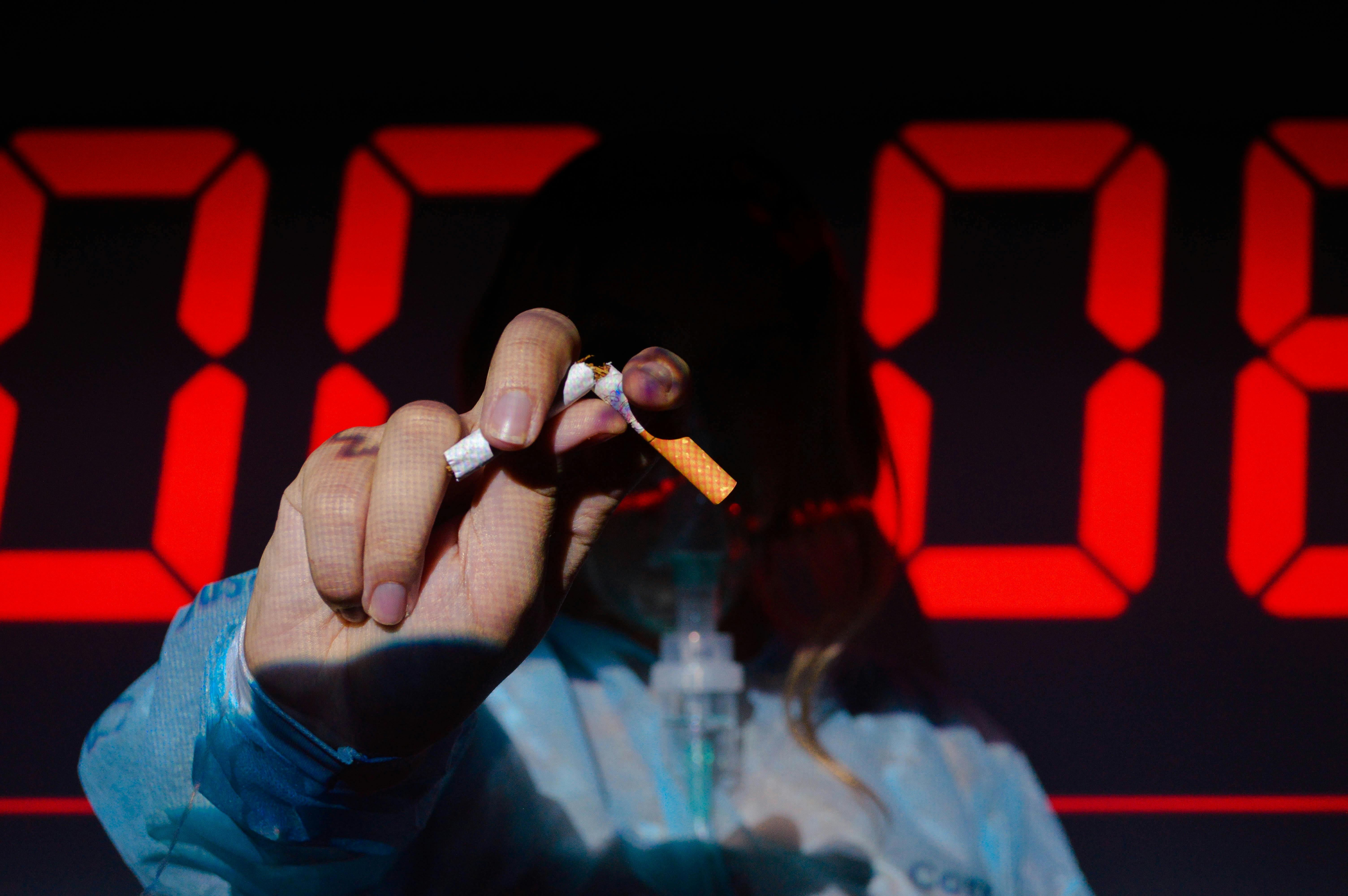 A hand holding a broken cigarette in front of a digital timer, highlighting the urgency of quitting smoking.
