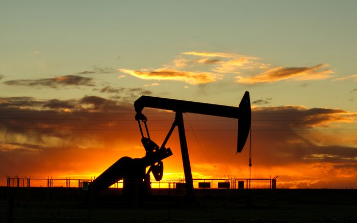 An oil pump jack silhouetted against an orange sunset sky.