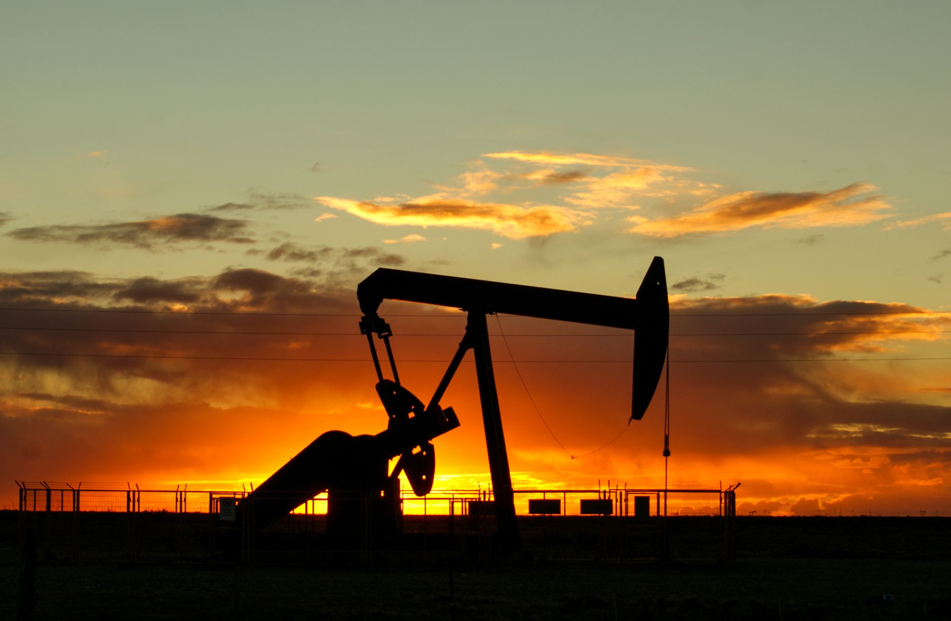 An oil pump jack silhouetted against a vivid sunset sky