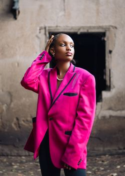 Fashionable woman posing in a bright pink blazer against a rustic background in Kumasi, Ghana.