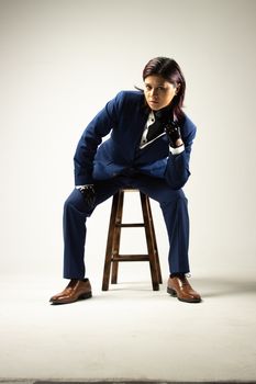 Stylish woman in blue suit sitting on stool with a confident pose.