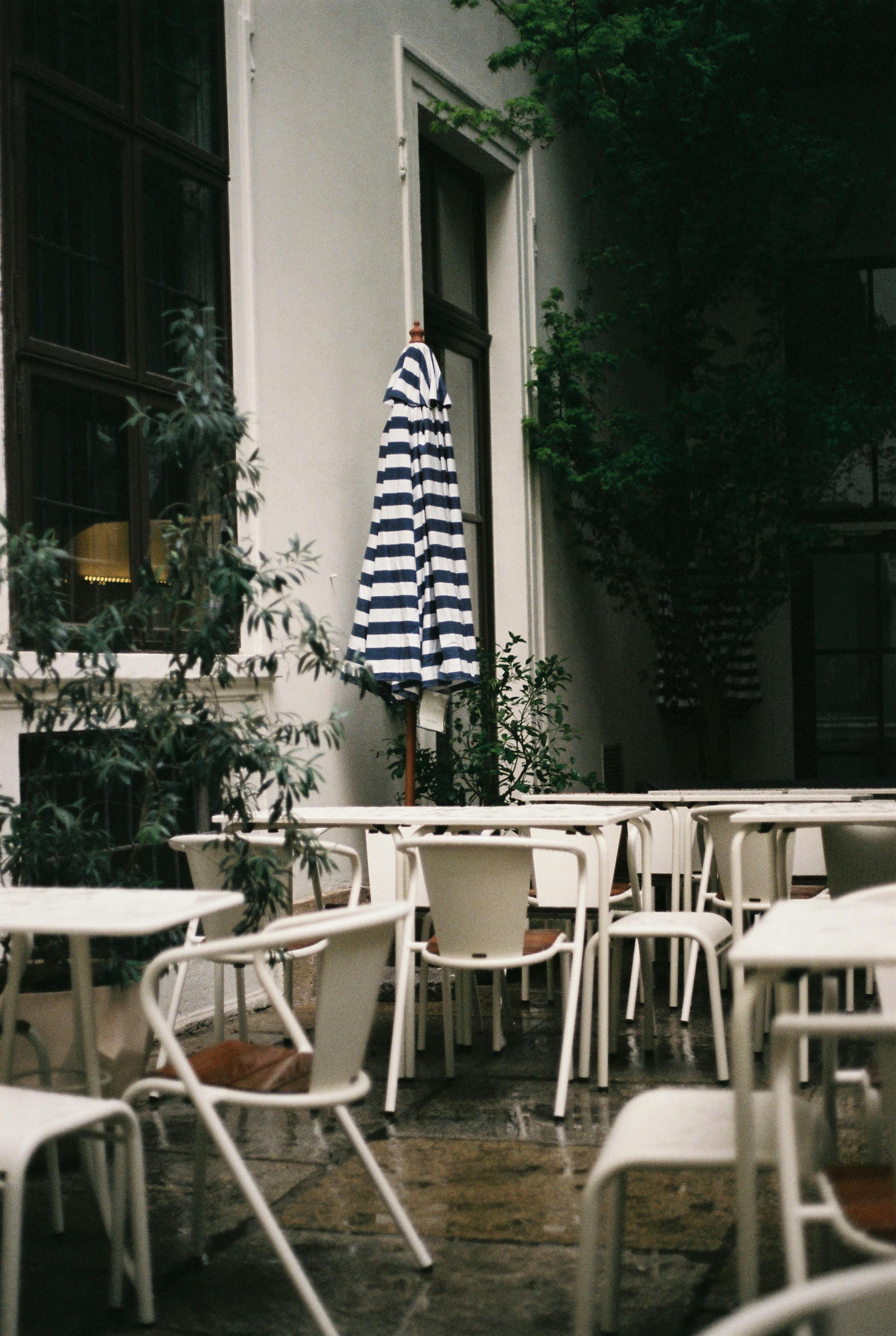 Tranquil outdoor café setting in Vienna featuring empty chairs, tables, and a striped umbrella.