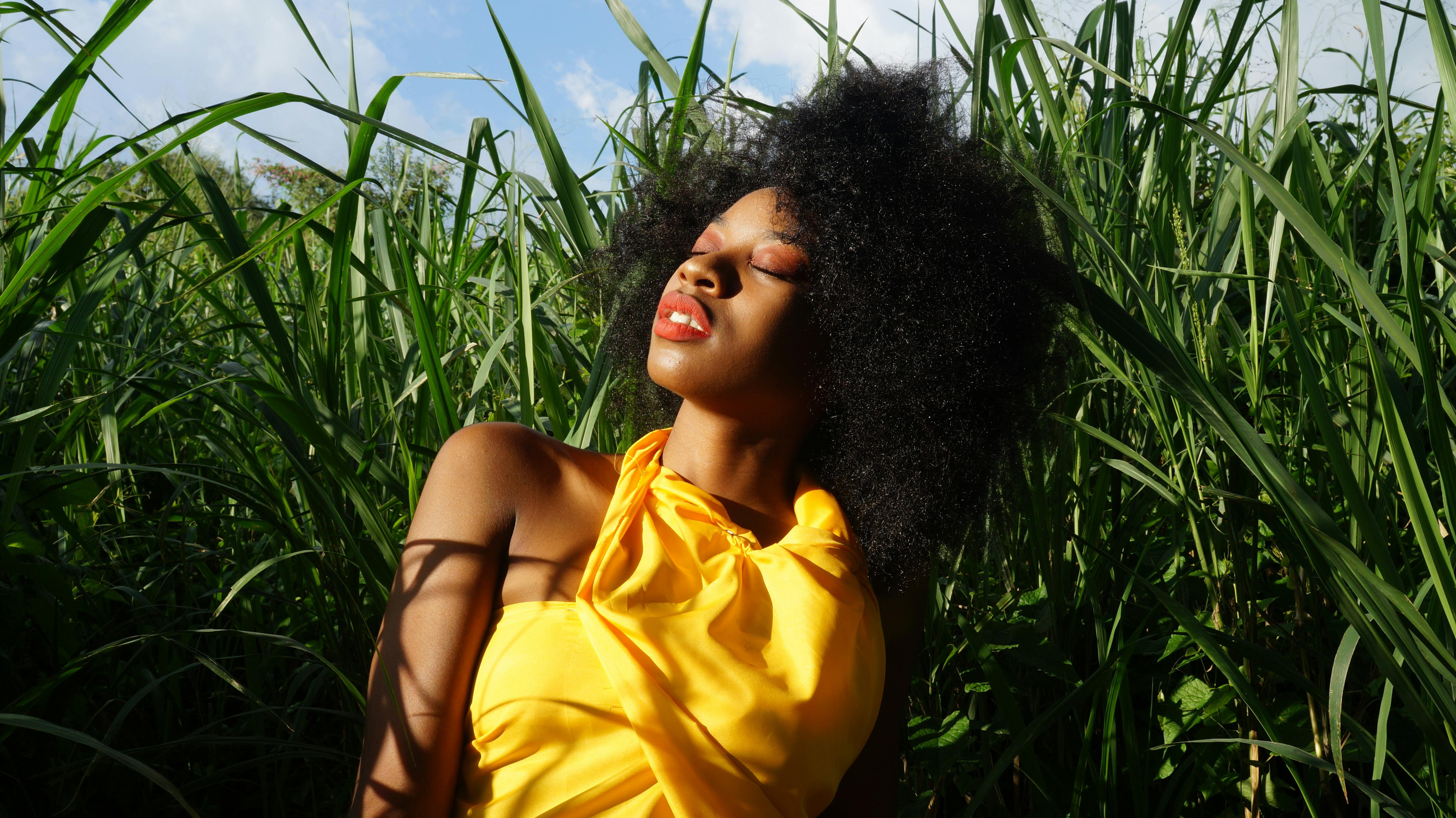 一位美丽的女子身穿黄色连衣裙，在郁郁葱葱的绿地上享受阳光