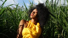 一位美丽的女子身穿黄色连衣裙，在郁郁葱葱的绿地上享受阳光