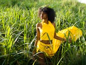 一位时尚女士身着鲜艳的黄色连衣裙，在高高的草丛中优雅地摆着姿势